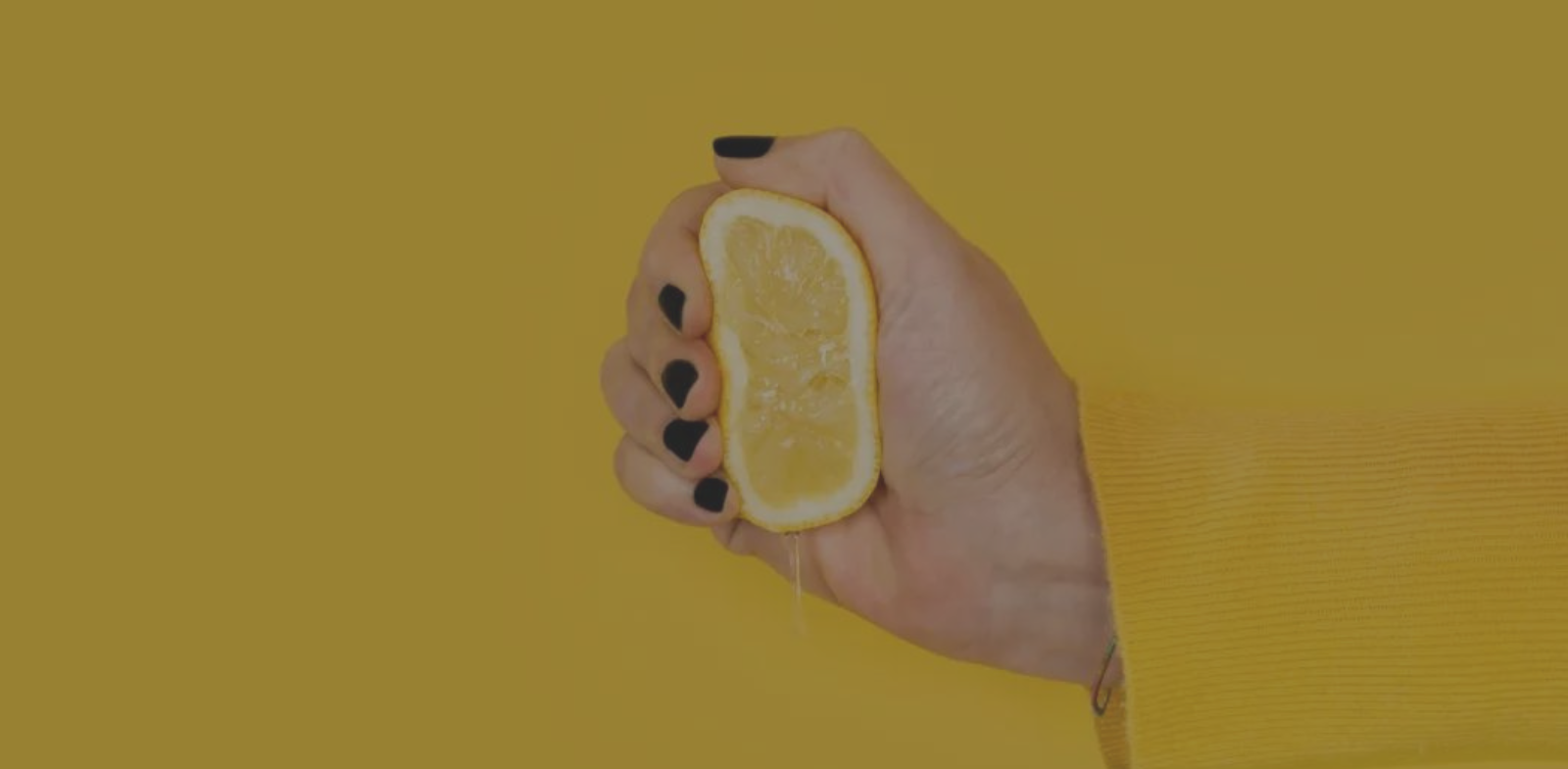 hand squeezing lemon on yellow background