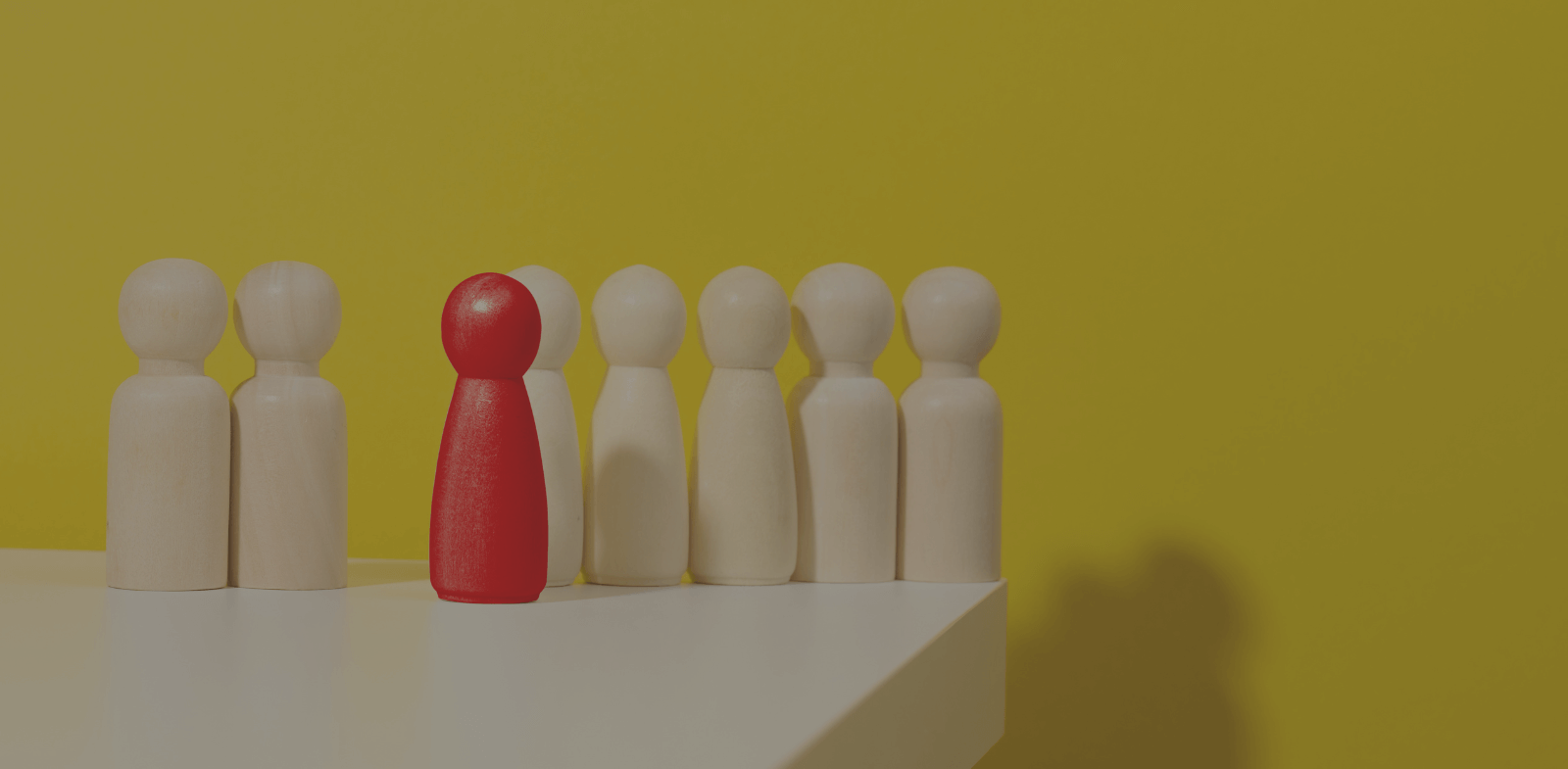red wooden figure standing out from plain wooden figures on yellow background