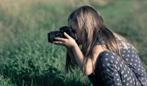 young girl holding DSLR camera in green grass field