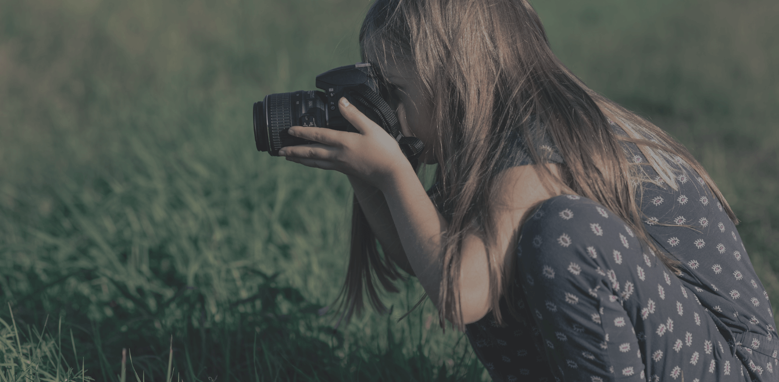 young girl holding DSLR camera in green grass field