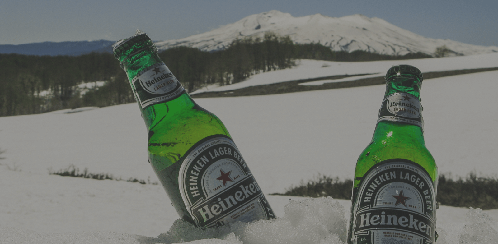Two bottles of Heineken Lager in the snow with mountain in background