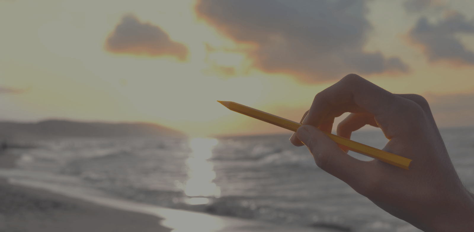 hand with pencil on sunset at the beach